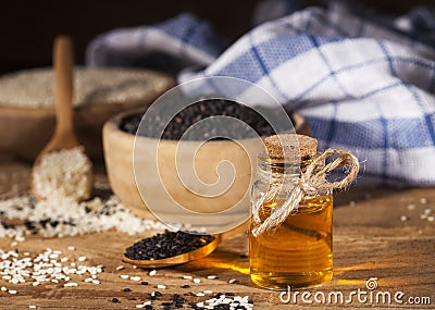 Fresh sesame oil in a glass bottle and white and black seeds in wooden bowls Stock Photo