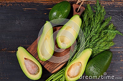 Fresh sliced avocados and dill on the wooden board. Raw ingredients for veggie healthy or diet dish on the black background Stock Photo