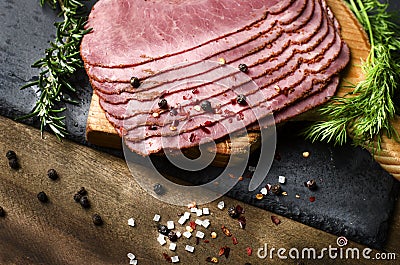 fresh sliced beef pastrami surrounded by herbs in wooden chopping board Stock Photo