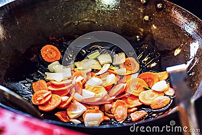 Fresh sliced vegetables: onion and carrot grilled with olive oil in pan or wok in the kitchen on hob. Concept of cooking. Stock Photo