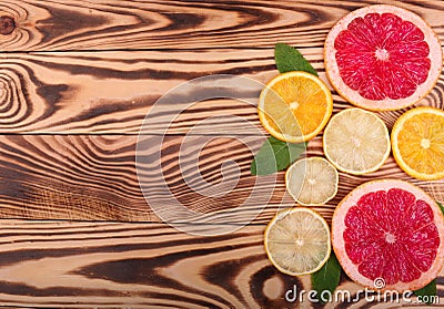 Fresh slices of juicy orange, ripe lemon, and organic grapefruit with leaves of mint on a wooden background, top view. Stock Photo