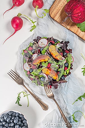 Fresh spring salad with rucola, lettuce, blueberries, radish, beet and slices of peach. White background with free text space. Top Stock Photo