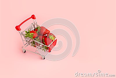 Fresh strawberry in shopping cart on pink background. Online shopping and Valentines Day minimalistic concept. Stock Photo