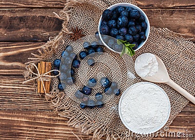 Fresh summer blueberry with leaf in the white bowl, flour in the bowl, wooden spoon on the brown wooden background Stock Photo