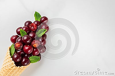 Fresh summer cherry berries with mint in waffle cone on white marble background. summer food concept. flat lay Stock Photo