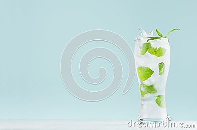 Fresh summer cold mint drink with green leaf, ice cubes, tonic in light soft pastel blue color background on white wood board. Stock Photo