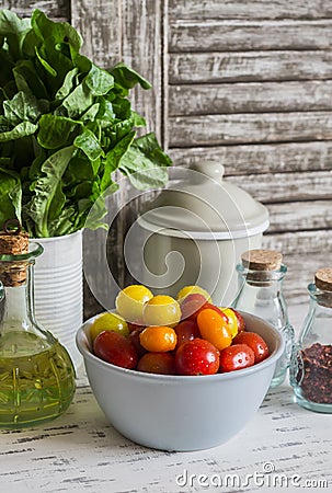 Fresh tomatoes in a ceramic bowl, green garden herb, olive oil and spices on a light rustic wood background. Stock Photo