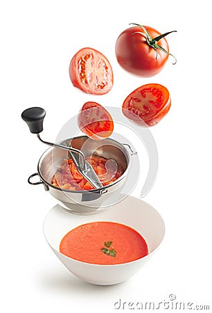 Fresh tomatoes flying, masher with crushed tomato and bowl with tomato cream Stock Photo