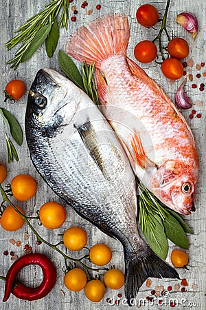 Fresh uncooked dorado or sea bream and red tilapia fish with lemon, aromatic herbs, vegetables and spices over grey background Stock Photo