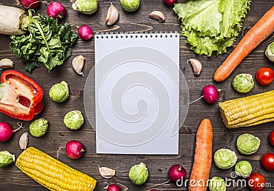 Fresh vegetables and herbs laid out around a notebook for recipes on wooden rustic background top view close up border, place for Stock Photo