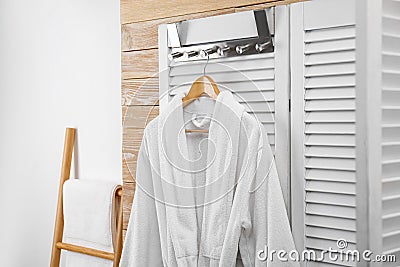 Fresh white bathrobe hanging on folding screen Stock Photo