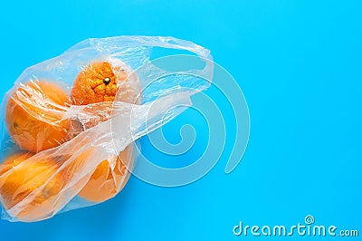 Fresh whole mandarins or oranges in polietilene bag on blue background. Fruit purchasing concept Stock Photo