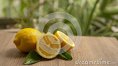 Fresh yellow ripe lemon round fruit and half sliced fruits with green leaf on brown wooden, blurry green tree background Stock Photo