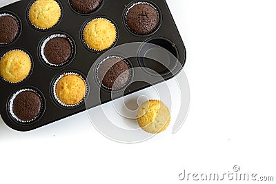 Freshly baked cupcake cakes in two varieties in a muffin tin, one standing outside, corner background faded to white, copy space, Stock Photo