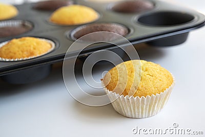 Freshly baked cupcake cakes in two varieties in a muffin tin, one standing outside, selected focus, narrow depth of field Stock Photo