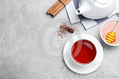 Freshly brewed rooibos tea, scattered dry leaves, honey and spices on grey table, flat lay. Space for text Stock Photo