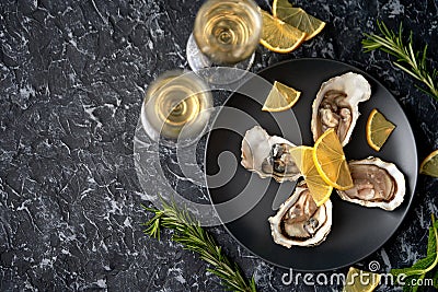 Freshly caught, opened oysters on a black plate with lemon slices, herbs and a glass of champagne on a dark stone background. Stock Photo