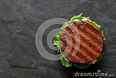 Freshly grilled plant based burger patty on bun with lettuce and sauce isolated on black slate. Top view. Copy space Stock Photo