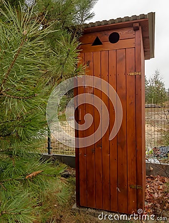 A freshly made wooden outhouse standing next to the fence among pines with long needles. Stock Photo