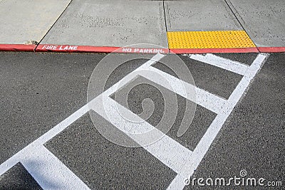 Freshly painted white crosswalk marking leading to a yellow painted ADA sidewalk access in a fire lane Stock Photo