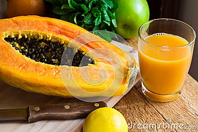 Freshly pressed papaya juice in glass, ripe halved fruit on wood cutting board Stock Photo