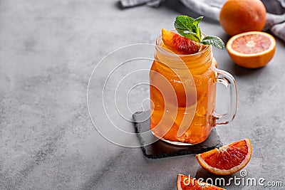 Freshly squeezed blood orange juice with ice, mint and a slice of fruit in a jar on a blue background with citrus fruits and Stock Photo