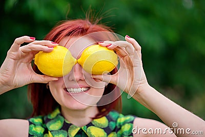 Freshness, healthy lifestyle and vitamins concept: smiling woman with red hair hiding her eyes behind two bright yellow lemons Stock Photo