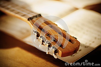The fretboard of an old acoustic guitar with metal strings lying on a wooden table next to sheets of sheet music. Solfeggio and Stock Photo