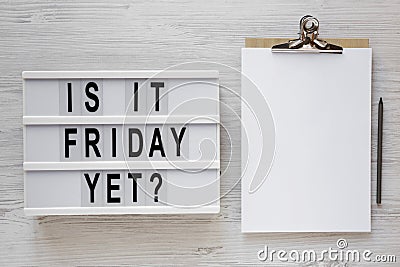 `Is it friday yet?` words on a modern board, clipboard with blank sheet of paper on a white wooden background, top view. Overhea Stock Photo