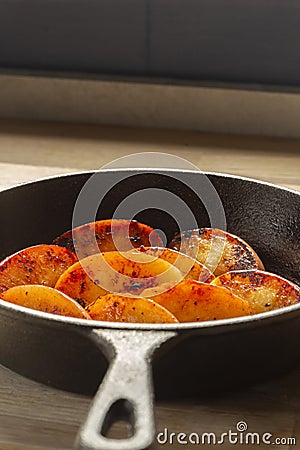 Fried apple, Pink Lady variety, in a cast iron frying pan. On a chopping board in a kitchen Stock Photo