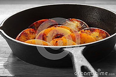 Fried apple, Pink Lady variety, in a cast iron frying pan. On a wooden chopping board Stock Photo