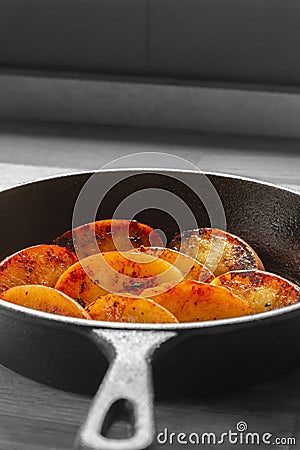 Fried apple, Pink Lady variety, in a cast iron frying pan. On a wooden chopping board Stock Photo