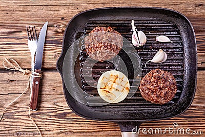 Fried burger beef cutlets with onion and garlic on grill pan with fork and knife Stock Photo