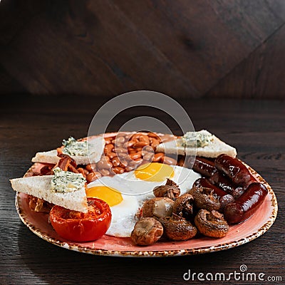 Fried champignons, fried eggs, juicy sausages, fried bacon, toast with butter and pickled beans in tomato sauce Stock Photo