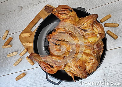 Fried chicken. On the table in a cast-iron pan, with a crisp, Golden crust. Bread sticks with sesame seeds. Wooden background Stock Photo