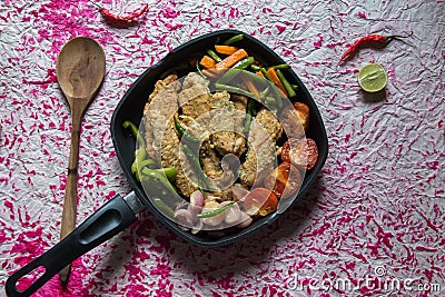 Fried chicken and stir fried vegetables in a black frying pan. Stock Photo