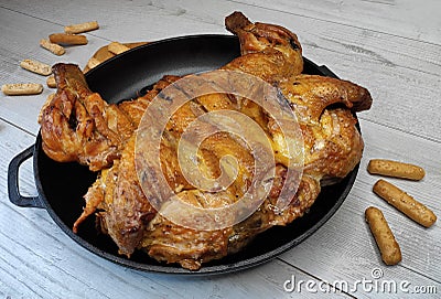 Fried chicken. On the table in a cast-iron pan, with a crisp, Golden crust. Bread sticks with sesame seeds. Wooden background Stock Photo