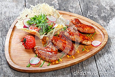 Fried chicken wings with fresh salad, grilled vegetables and bbq sauce on cutting board on wooden background Stock Photo