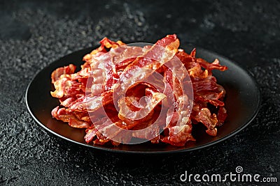 Fried crunchy Streaky Bacon pieces in a black plate Stock Photo