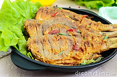 Fried fish carp sazan on a cast-iron frying pan with lettuce leaves Stock Photo