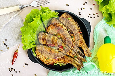 Fried fish carp sazan on a cast-iron frying pan with lettuce leaves on a light background. Stock Photo