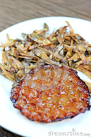 Fried giant catfish and pile of Deep fried small fishes Minnow fish Traditional Thai recipes in white dish on rustic wood Stock Photo