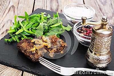 Fried liver, fresh arugula on black stone plate Stock Photo