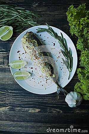 Fried mackerel served on a plate, decorated with spices, herbs and vegetables. Proper nutrition. View from above. Dark wooden Stock Photo