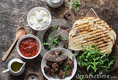 Fried meatballs, tomato sauce, mozzarella, arugula, grilled bread hot sandwiches ingredients on a wooden table, top view. Deliciou Stock Photo