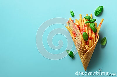 Fried potatoes in waffle cones on blue background. Hot salty french fries with tomato sauce, basil leaves. Fast food Stock Photo