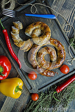 Fried sausage with herbs and spices, wooden background. Ring of baked homemade sausage. Served on a wooden board with a fork, Stock Photo