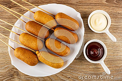 Fried sausages on skewers in white dish, sauce boats with mayonnaise and ketchup on table. Top view Stock Photo