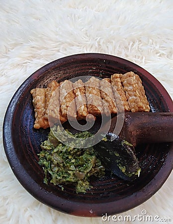 Fried tempeh and green chili sauce are placed on a clay mortar. Tempe is a favorite and cheap food in Indonesia. Stock Photo