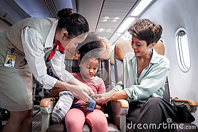 Friendly air hostess take care kid passenger on airplane, flight attendant teach curly hair African girl to use seat belt during Stock Photo